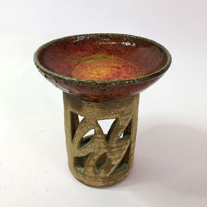 May include: A handcrafted ceramic pedestal bowl with a vibrant red and yellow interior. The bowl sits atop a cylindrical base with decorative cutouts. The rim has a textured, green edge. This unique piece is ideal for home decor.