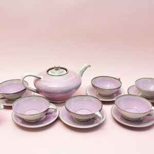 May include: A pink and white tea set with a teapot, creamer, and six cups and saucers.