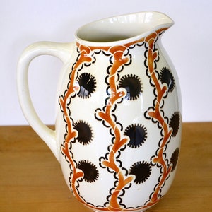 May include: White ceramic pitcher with a brown and black floral design. The pitcher has a rounded body and a curved handle.