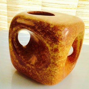 May include: A brown ceramic vase with a square shape and cut-out openings. The vase has a speckled glaze.