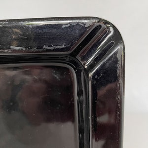 K&ouml;nnte beinhalten: Schwarzer Aschenbecher aus Glas mit quadratischer Form und abgeschr&auml;gter Kante. Der Aschenbecher hat eine glatte, gl&auml;nzende Oberfl&auml;che.