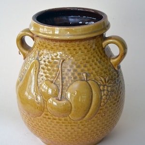 Könnte beinhalten: Eine braune Keramikvase mit zwei Henkeln und einer strukturierten Oberfläche. Die Vase ist mit einer Birne, Kirschen und einem Pfirsich verziert.