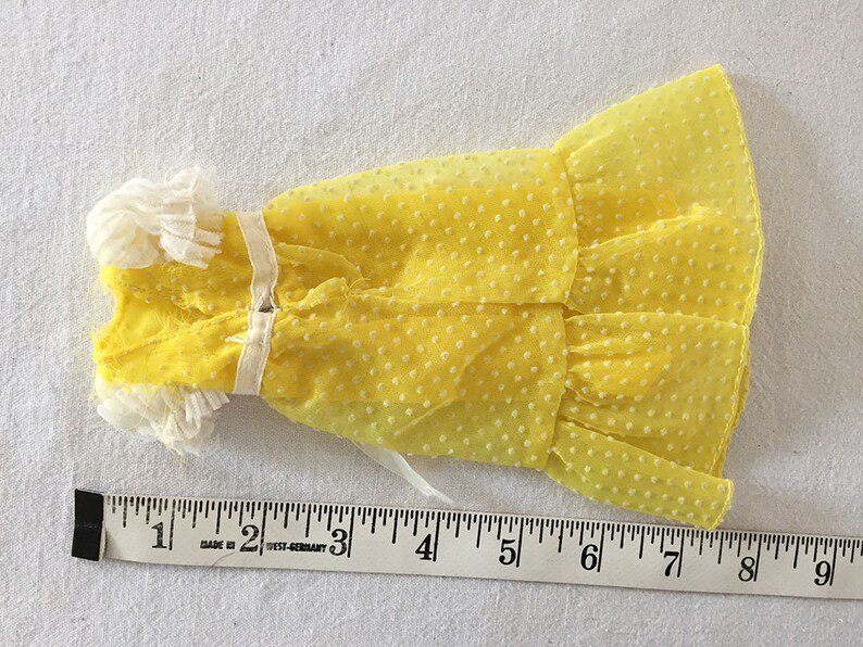May include: A yellow polka dot dress with white lace trim. The dress is about 7 inches long.