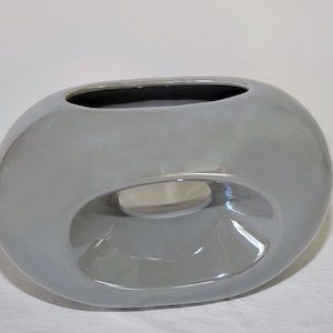 May include: A gray ceramic vase with a unique, organic shape. The vase has a large opening at the top and a smaller opening on the side.