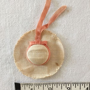 May include: A small straw hat with a peach-colored ribbon. The hat is about 1 inch in diameter.