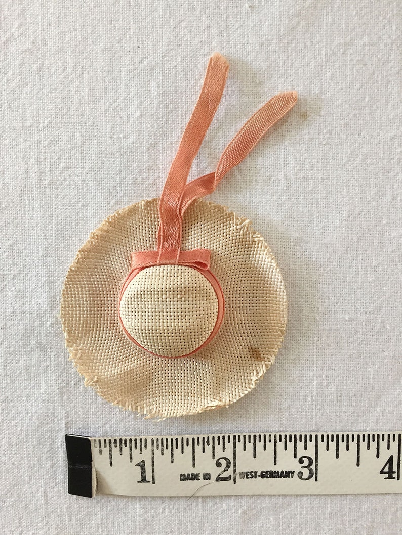 May include: A small straw hat with a peach-colored ribbon. The hat is about 1 inch in diameter.