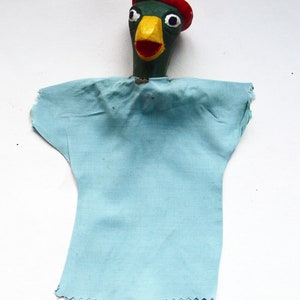 May include: A green and yellow puppet with a red hat and a blue fabric body. The puppet has a large beak and large eyes.