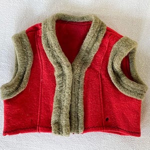 May include: A red fleece vest with a brown faux fur collar and trim. The vest has a V-neck and is sleeveless.