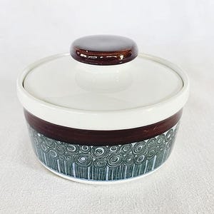 May include: A ceramic sugar bowl with a lid. The bowl is white with a dark brown band and a decorative pattern of blue and green swirls. The lid has a dark brown knob.