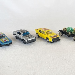 May include: Four toy cars in a row. A blue car with yellow and red stripes, a silver car with black flames, a yellow car with a racing stripe, and a green vintage car with gold accents.