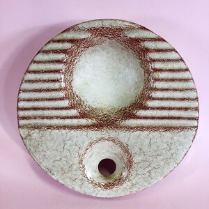 May include: A white ceramic ashtray with a brown glaze and a round shape. The ashtray has a deep well in the center and a small hole on the side.