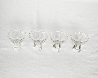 May include: Four clear glass footed bowls with a geometric pattern. The bowls are arranged in a row on a white surface.