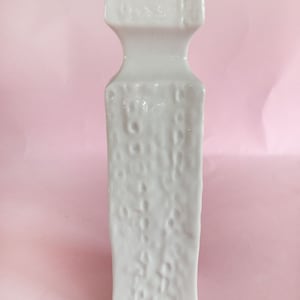 May include: White ceramic vase with a textured surface. The vase has a square base and a rectangular body with a slightly flared top.