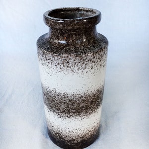 Puede incluir: Un jarrón de cerámica blanco y marrón con un esmalte moteado. El jarrón tiene una forma cilíndrica y una boca ancha.