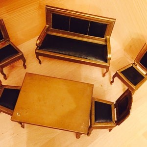 May include: A miniature gold-painted furniture set with a black leather sofa, four chairs, and a table. The set is made of wood and has a vintage look.