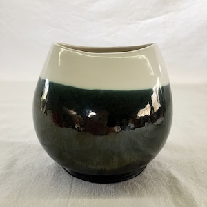 May include: A white and green ceramic vase with a rounded, slightly asymmetrical shape. The vase has a glossy finish and a wide opening.