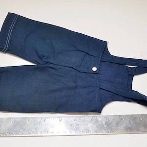 May include: A pair of dark blue denim overalls with white stitching. The overalls have a button closure and adjustable straps.