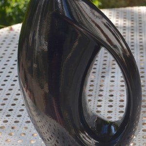 May include: A black ceramic vase with a unique, abstract design. The vase has a smooth, glossy finish and a large opening at the top.