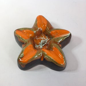 Puede incluir: Un cenicero de cerámica con forma de estrella de mar con un esmalte marrón, verde y naranja.