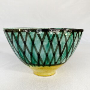 May include: A green ceramic bowl with a black and white diamond pattern. The bowl has a yellow rim.