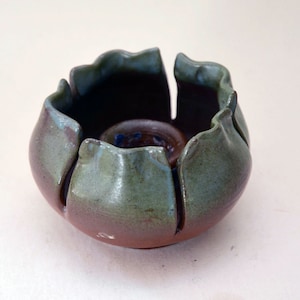 May include: A handmade ceramic candle holder with a flower-like design. The holder is glazed in shades of green and brown.