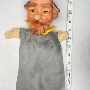 Peut inclure: Une marionnette grise avec une tête chauve, une barbe et une moustache brunes. La marionnette a des yeux jaunes et un col jaune. La marionnette mesure 30 cm de haut.