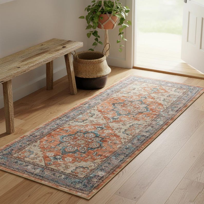 Peut inclure: Un tapis rectangulaire avec un motif vieilli et vintage. Le tapis pr&eacute;sente un motif central dans des tons orange et bleu, encadr&eacute; par une bordure bleue. Il est pos&eacute; sur un sol en bois, ajoutant de la chaleur &agrave; l'espace.