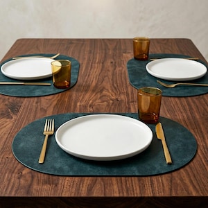 May include: A dining table set with four place settings. Each place setting features a white plate, gold cutlery, and a brown glass on a teal placemat. The table is made of dark wood.