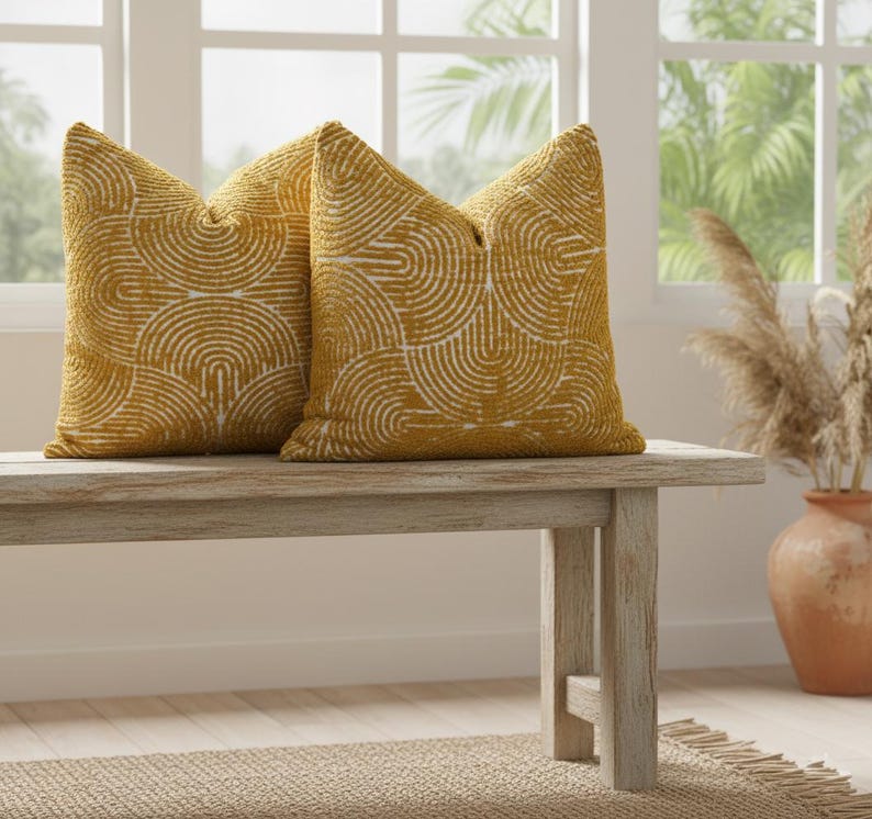 May include: Two mustard-yellow throw pillows with a white, semi-circular pattern. The pillows are placed on a light-colored wooden bench. The pillows add a decorative touch to any living space.