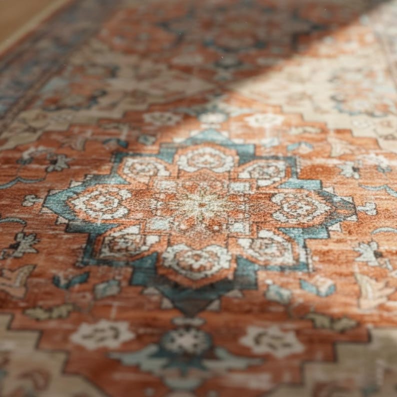 Peut inclure: Gros plan sur un tapis &agrave; motifs avec un motif de m&eacute;daillon central. Le tapis pr&eacute;sente une palette de couleurs chaudes d'orange rouille, de sarcelle et de cr&egrave;me, avec des motifs floraux et g&eacute;om&eacute;triques complexes. La texture du tapis est visible, sugg&eacute;rant une construction tiss&eacute;e.