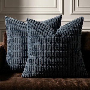 May include: Three navy blue corduroy throw pillows with a textured, ribbed design. The pillows are square-shaped and rest on a brown sofa. The pillows have a soft, inviting appearance, perfect for adding comfort and style to any living space.