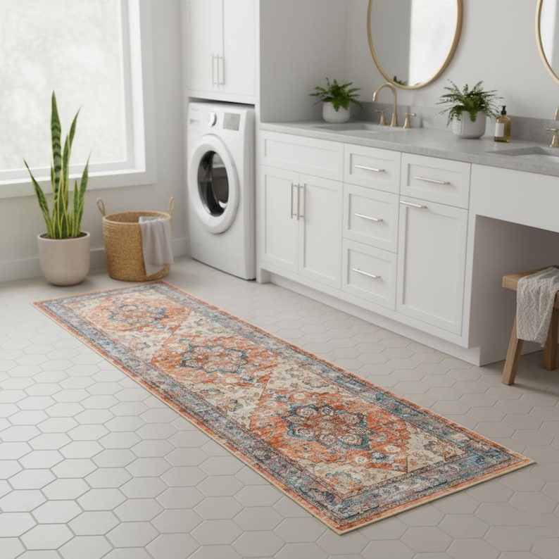 Peut inclure: Un long tapis rectangulaire avec un motif complexe et vieilli dans des tons d'orange, de bleu et de cr&egrave;me. Le tapis est pos&eacute; sur un sol carrel&eacute; gris clair dans une salle de bain, avec une machine &agrave; laver et des meubles blancs en arri&egrave;re-plan.