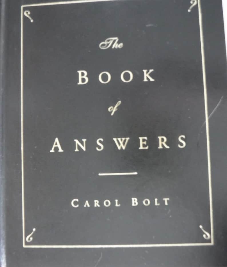 K&ouml;nnte beinhalten: Ein schwarzes Hardcover-Buch mit dem Titel "The Book of Answers" von Carol Bolt. Der Titel und der Name des Autors sind in wei&szlig;er Schriftart gehalten. Der Einband hat einen dekorativen Rahmen.