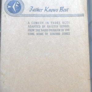 May include: Vintage book cover for "Father Knows Best," a comedy in three acts. The cover is a light tan color with blue text and a blue and white circular logo. The text includes the title, author, and publisher.