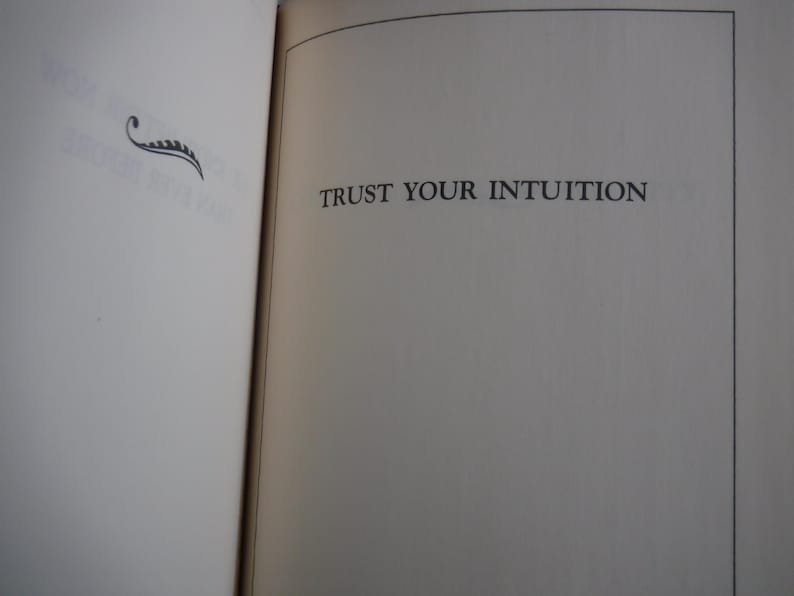 K&ouml;nnte beinhalten: Offene Buchseiten mit dem Text "TRUST YOUR INTUITION" in einer Serifenschrift. Eine dekorative schwarze Verzierung befindet sich in der oberen linken Ecke. Die Seiten sind cremefarben mit einer leichten Textur.