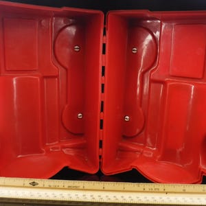 May include: Open red plastic case with a hinged design. The interior features molded compartments and circular indentations. A ruler is at the bottom of the image.