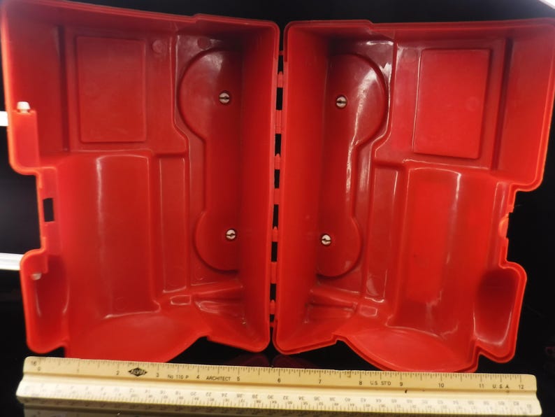 May include: Open red plastic case with a hinged design. The interior features molded compartments and circular indentations. A ruler is at the bottom of the image.