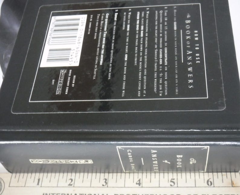 K&ouml;nnte beinhalten: Ein schwarzes Hardcover-Buch mit dem Titel "The Book of Answers" mit wei&szlig;em Text. Das Buch hat eine rechteckige Form und scheint geschlossen zu sein. Der Buchr&uuml;cken tr&auml;gt den Titel und den Namen des Autors. Das Buch liegt auf einer Oberfl&auml;che.