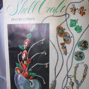 Puede incluir: La portada de un libro antiguo titulado "The Book of Shell Craft Instruction". La portada presenta ilustraciones de joyas y artesanías basadas en conchas, incluyendo collares y elementos decorativos, con una etiqueta de precio en la esquina superior derecha.