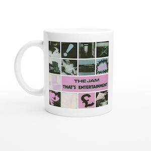 May include: White ceramic mug featuring a collage of black and white images with a pink banner that reads "THE JAM THAT'S ENTERTAINMENT". The mug has a white handle and a glossy finish.