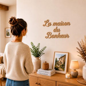 Peut inclure: Une enseigne murale en bois brun clair présentant le texte en cursive La maison du Bonheur fixé sur un mur uni. L'enseigne se compose de trois lignes distinctes de lettrage script, chacune avec une finition lisse, placée au-dessus d'une console.
