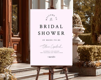 Könnte beinhalten: Ein hellrosa Schild auf einer Holzstaffelei. Auf dem Schild steht "Willkommen zur Bridal Shower von Bride-to-be Olivia Copeland" mit Datum und Hashtag #mrsliv.
