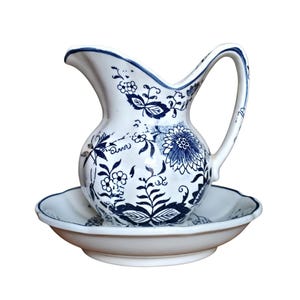 May include: A white ceramic jug and basin set, decorated with blue floral motifs. The jug features a curved handle and spout, while the basin has a scalloped edge. The floral design includes flowers, leaves, and vines, offering a classic, vintage appearance.