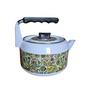 May include: White enamel tea kettle with a black handle and a floral pattern in green, yellow, and brown. The kettle has a spout and a lid with a black knob. A vintage kitchenware item.