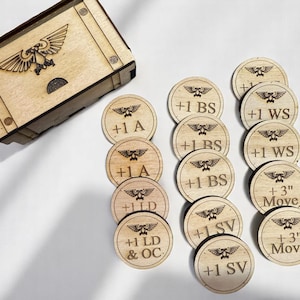 May include: Wooden game tokens with etched symbols and text, including "+1 BS", "+1 WS", and "+3" Move". A wooden box with a matching design is also present. The tokens are approximately 1.5 inches in diameter.
