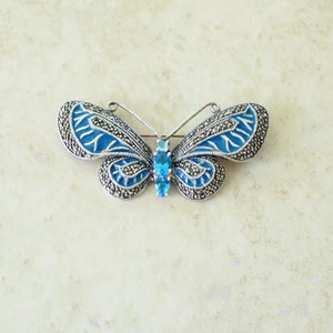 May include: A silver-toned butterfly brooch with blue enamel wings and marcasite accents. The brooch features a central blue gemstone and is designed to be worn as a decorative accessory.