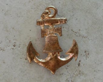 May include: A gold-toned metal pin shaped like a ship anchor with a Liberty Bell integrated into the center. The bell features embossed text that is partially visible, and the entire piece has a textured, metallic finish with a loop at the top.