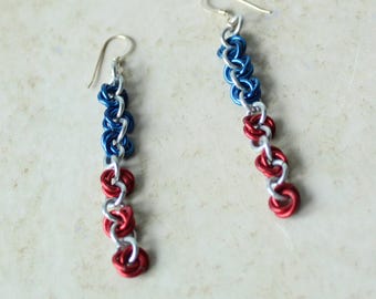 May include: A pair of dangle earrings featuring a chainmaille design with interlocking silver, blue, and red metal rings. Each earring hangs from a simple silver-toned hook wire, creating a vertical pattern of alternating colored metal links.
