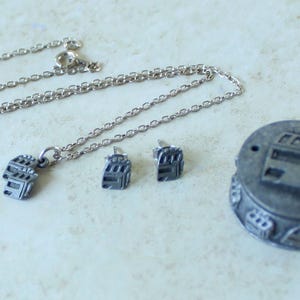 May include: A silver-toned jewelry set featuring a necklace with a pendant, matching earrings, and a small round box. The pendant and earrings have a slot machine design. The box also has a slot machine design on the lid.