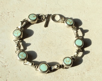 May include: A silver link bracelet featuring six circular bezel-set turquoise stones with brown matrix veining. The bracelet is secured with a toggle clasp consisting of a silver bar and a circular ring, connected by small silver spheres.